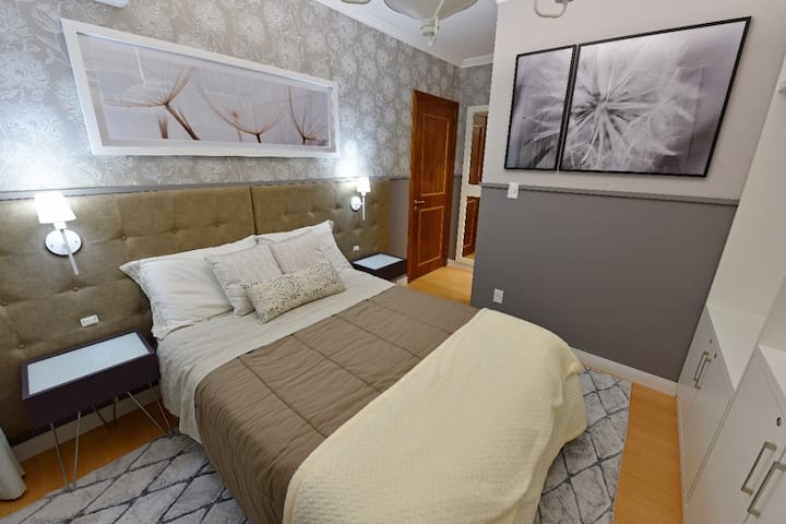 Suíte com cama de casal, armários para guardar as roupas, TV smart, ar-condicionado e escrivaninha.