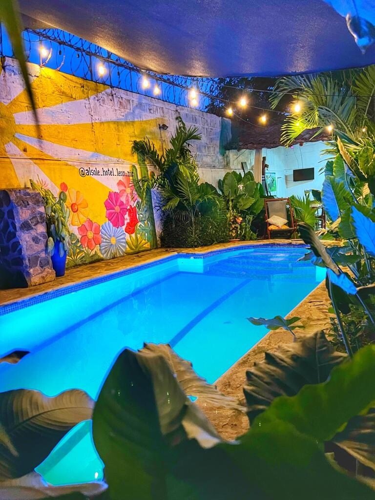 A private pool is surrounded by lush greenery and vibrant tropical plants. Soft lighting enhances the serene atmosphere, while a mural featuring colorful flowers adorns the wall behind the pool, creating an inviting environment for relaxation.