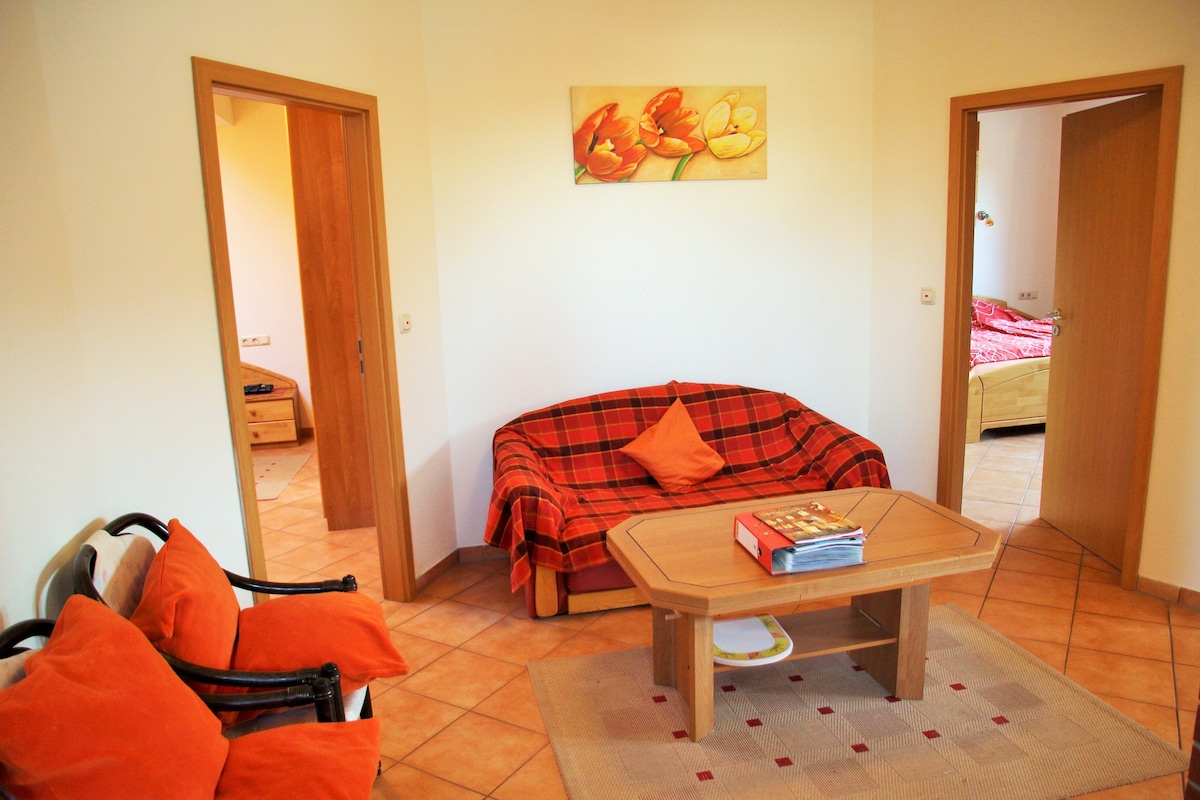 A inviting living area is featured, showcasing a cozy red and orange plaid sofa with an accent pillow. A wooden coffee table is centered on a light rug, while a piece of floral wall art hangs above. Two doorways lead to adjacent rooms.