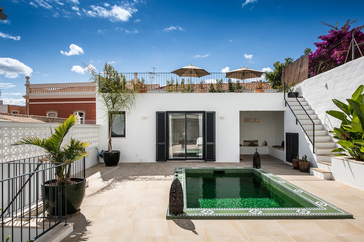 A serene outdoor space is highlighted by a plunge pool surrounded by elegant tiles. The area features a spacious terrace with sun umbrellas and lush greenery. Modern design elements are complemented by traditional décor, creating an inviting environment for relaxation and socializing.