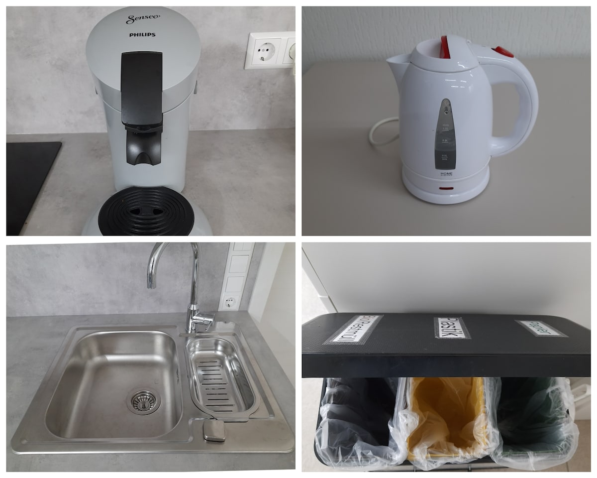 A modern kitchen area showcases a coffee maker and an electric kettle. A stainless steel sink is visible, along with a countertop featuring organized recycling bins in various colors. The minimalist design emphasizes functionality and convenience.