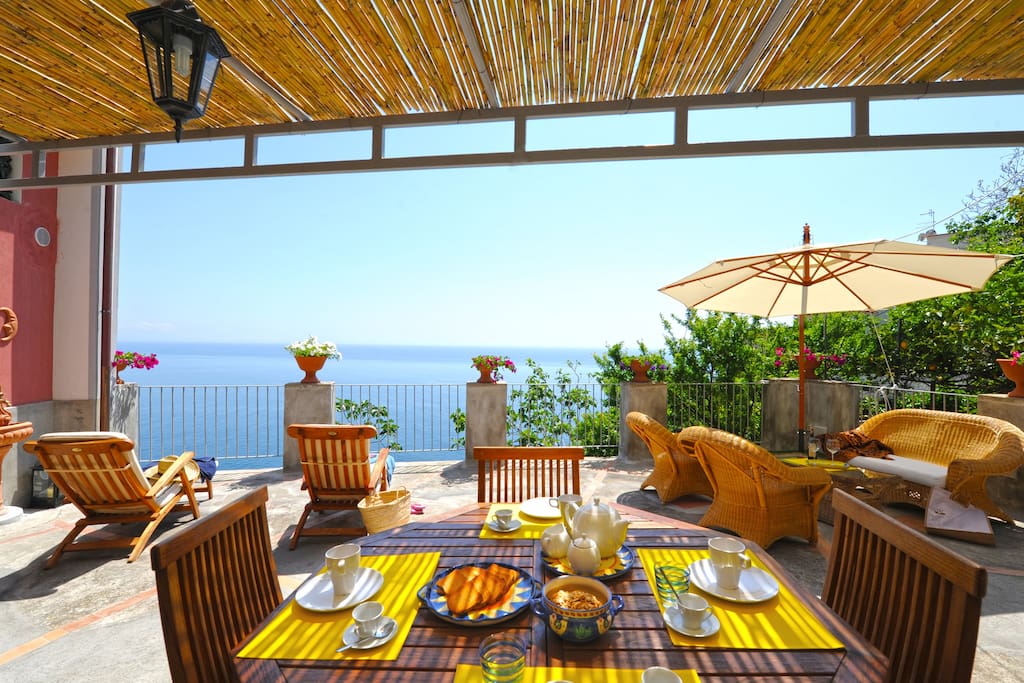 Large terrace surrounded by greenery with wicker sofas, sun beds, sea view