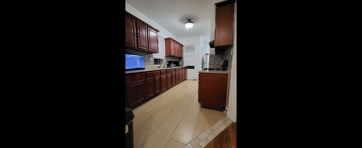 A contemporary kitchen features dark wooden cabinets lining the walls, providing ample storage. A light-colored countertop contrasts with the cabinetry. Modern appliances, including a refrigerator and stovetop, are visible, and tile flooring offers a clean and functional space for cooking.