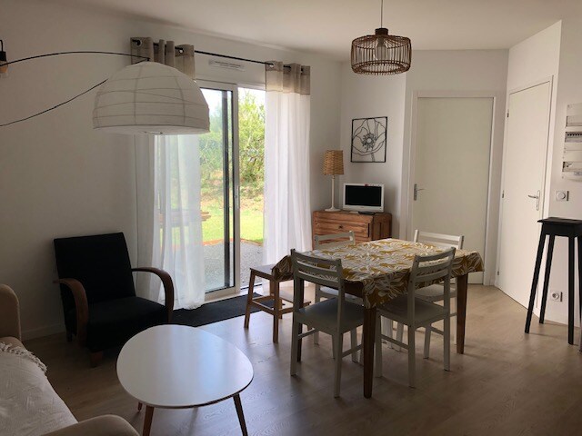 A light-filled living space features a glass door leading to the garden, surrounded by modern furniture. A dining table with seating for six is complemented by a wooden sideboard. A comfortable armchair and a minimalistic coffee table offer additional seating options.
