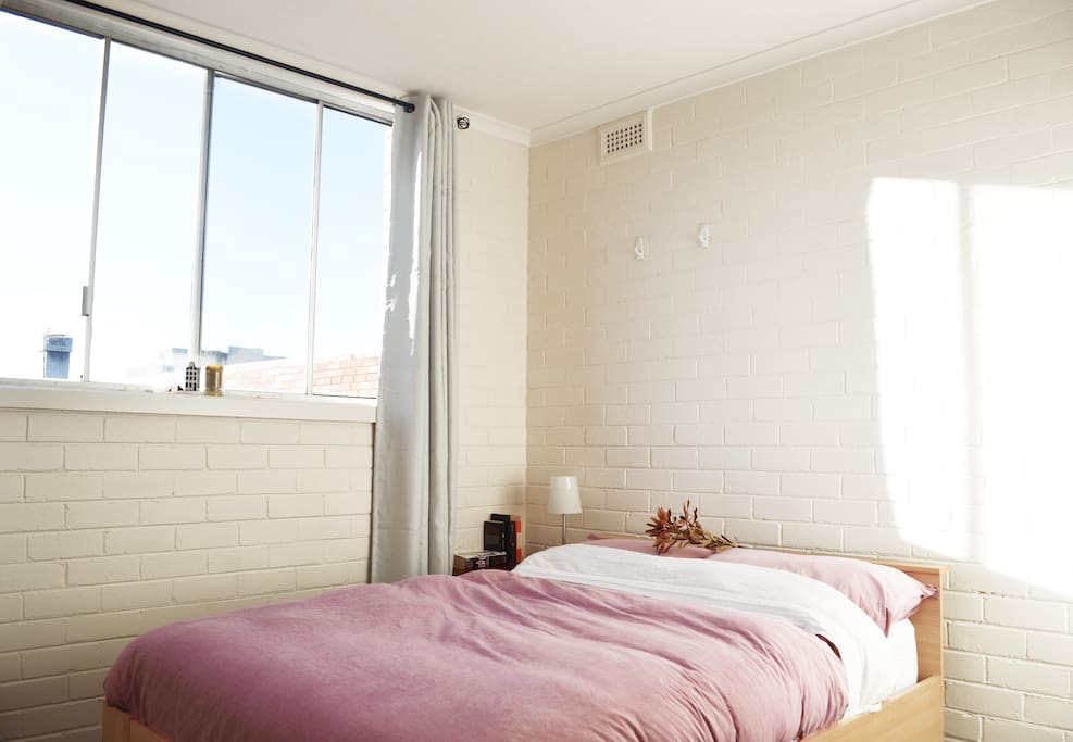 The bright bedroom filled with natural light looks out onto rooftops.
