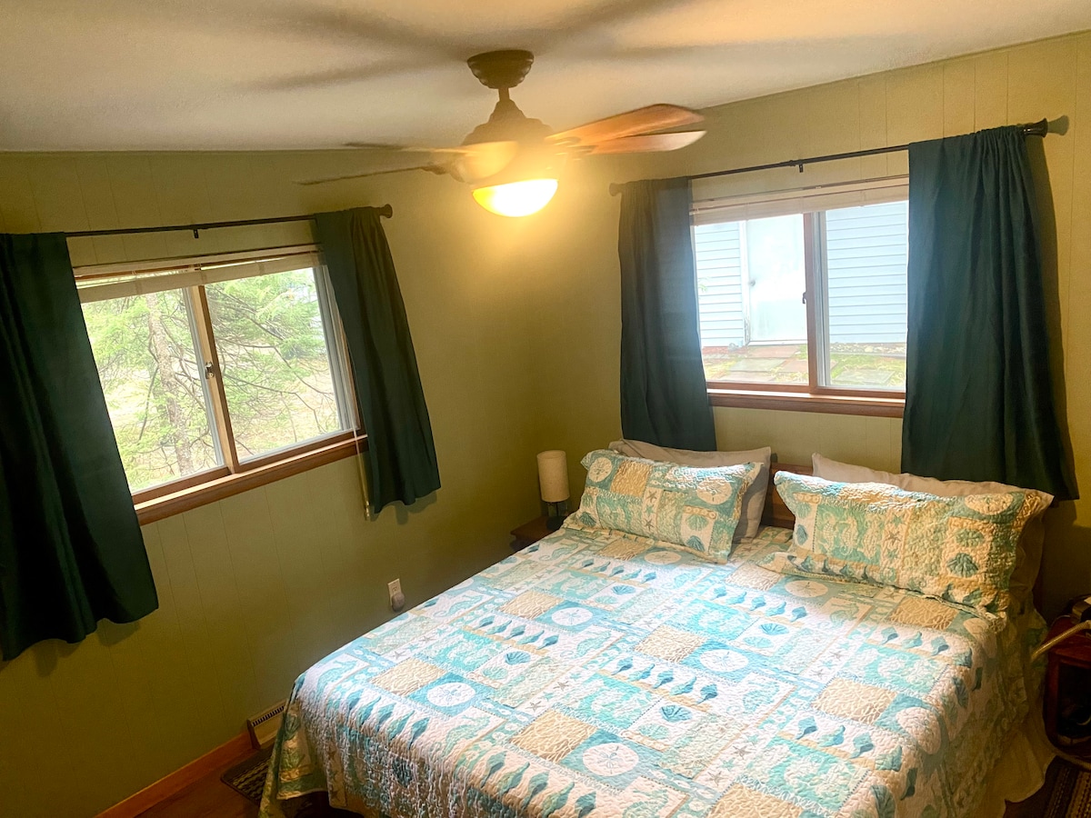 Dormitorio verde con espuma viscoelástica tamaño king, ventilador de techo, mesa auxiliar con lámpara.  Las lámparas tienen puertos y tomas eléctricas.