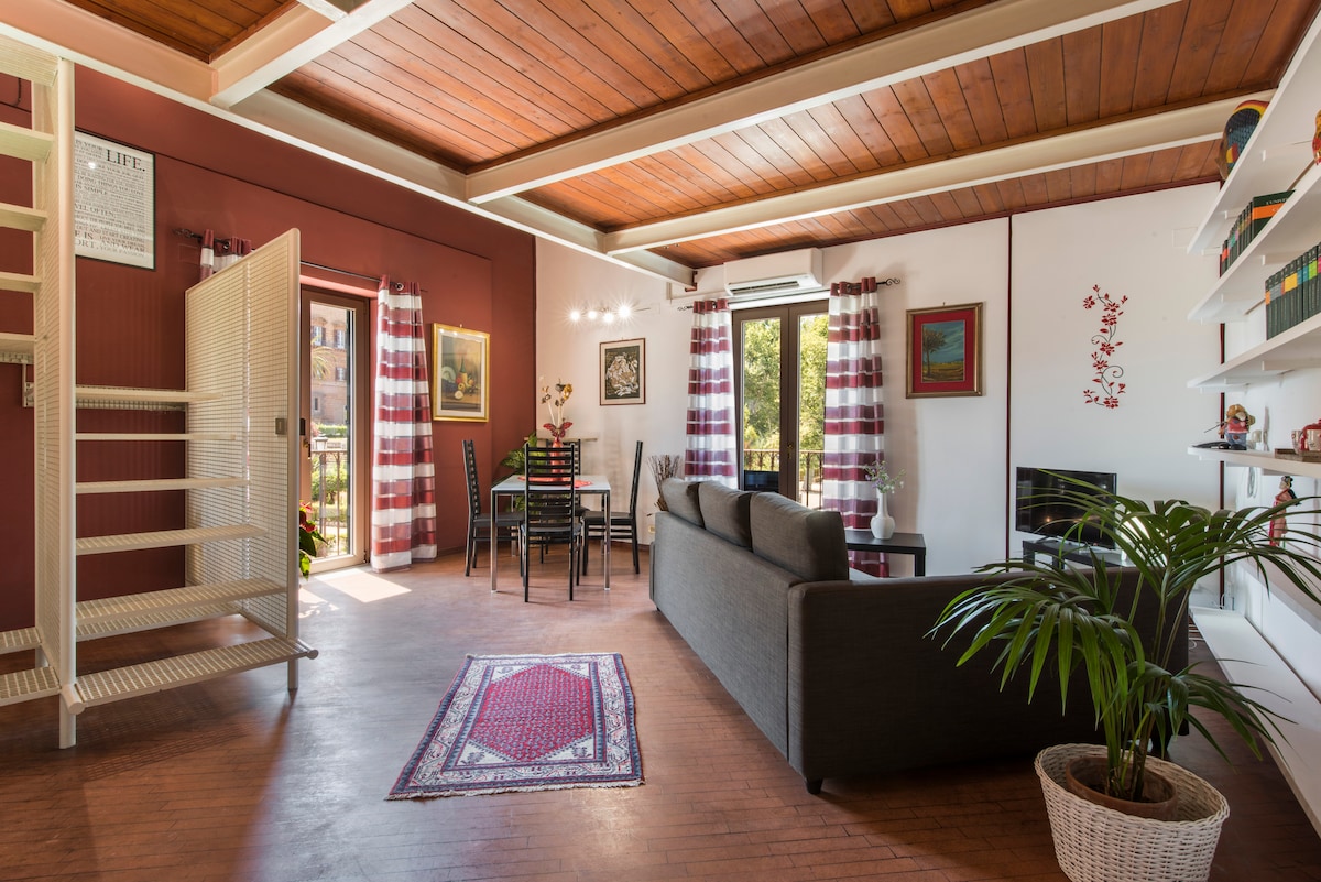 A modern living space is showcased, featuring a comfortable sofa and a dining table surrounded by chairs. Large windows provide natural light, complemented by elegant curtains. A plant adds a touch of greenery, while wooden beams enhance the ceiling's character.