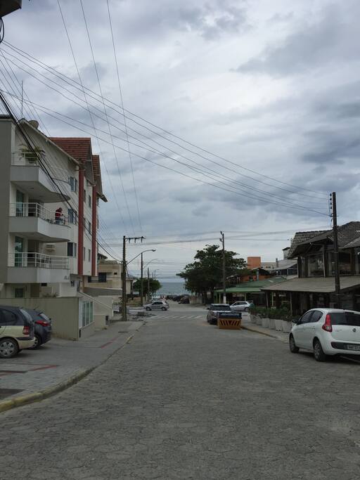 Visão da rua, com restaurante na esquina e praia ao fundo
