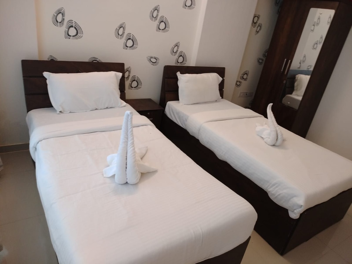 The sleeping area features two neatly arranged beds that are covered with crisp white linens. Each bed is complemented by a decorative towel creation resembling a swan. A minimalist design is displayed on the wall, enhancing the room's overall aesthetic.