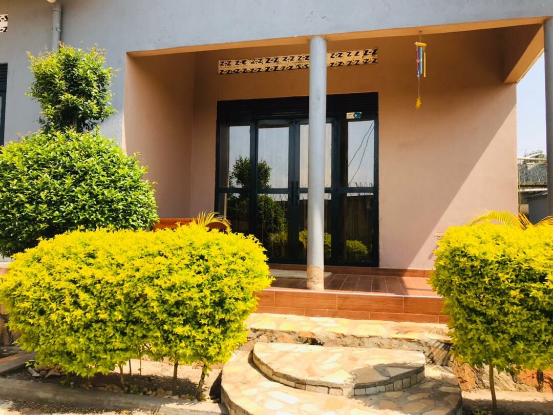 A charming entrance to the house is framed by neatly trimmed green shrubs and vibrant yellow foliage. The pathway leads to a covered porch with large glass doors, providing a view into the interior. Natural light enhances the welcoming appearance of the entrance.