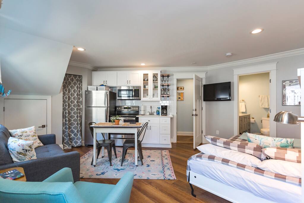 Studio includes a full kitchen, sitting area, small kitchen table, queen sized bed, tv, and bathroom.