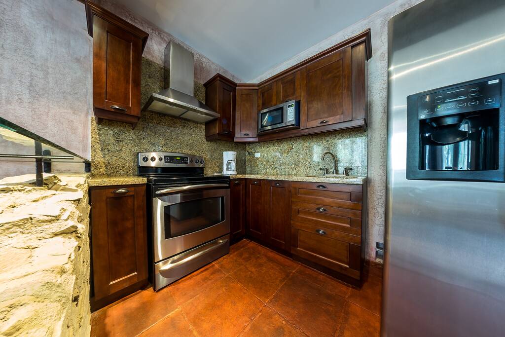 Cocina equipada, licuadora, cafetera, estufa con horno, horno miccroondas, refrigerador y detalle entre la división de espacios.