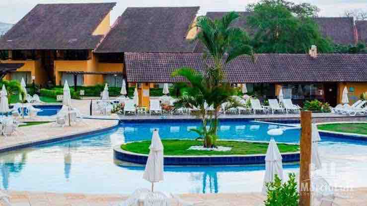 A wide view of the resort's pool area is displayed, featuring inviting blue water surrounded by a sun terrace. Several lounge chairs and umbrellas are arranged around the pool, complemented by tropical plants and landscaped gardens in the background.