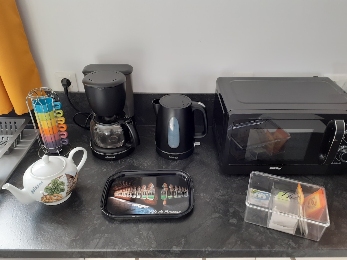 A countertop is displayed featuring a coffee maker, electric kettle, and microwave, providing essential kitchen amenities. A decorative tray is visible with a themed design, and a clear container holds various tea bags. Colorful utensils are arranged neatly in a holder nearby.