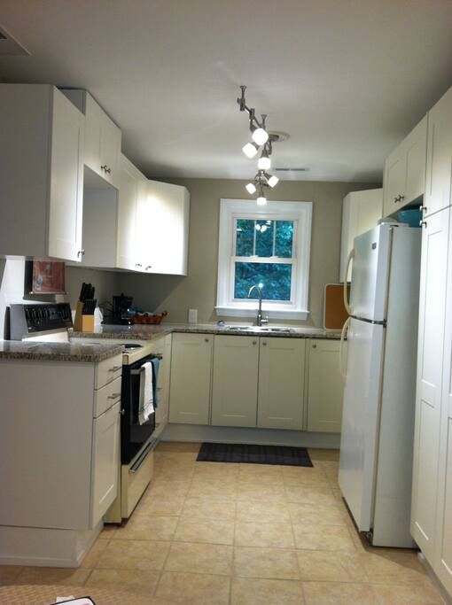 Prepare a meal in this Ikea Kitchen with Granite counter tops, track lighting, ceramic tile floor, Stainless Steel dishwasher, microwave, stove, refrigerator, coffee pot, tea kettle, cookware.