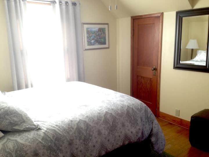 Upper level south bedroom is bright with morning sun. There are hardwood floors, queen-size bed and light-darkening draperies.