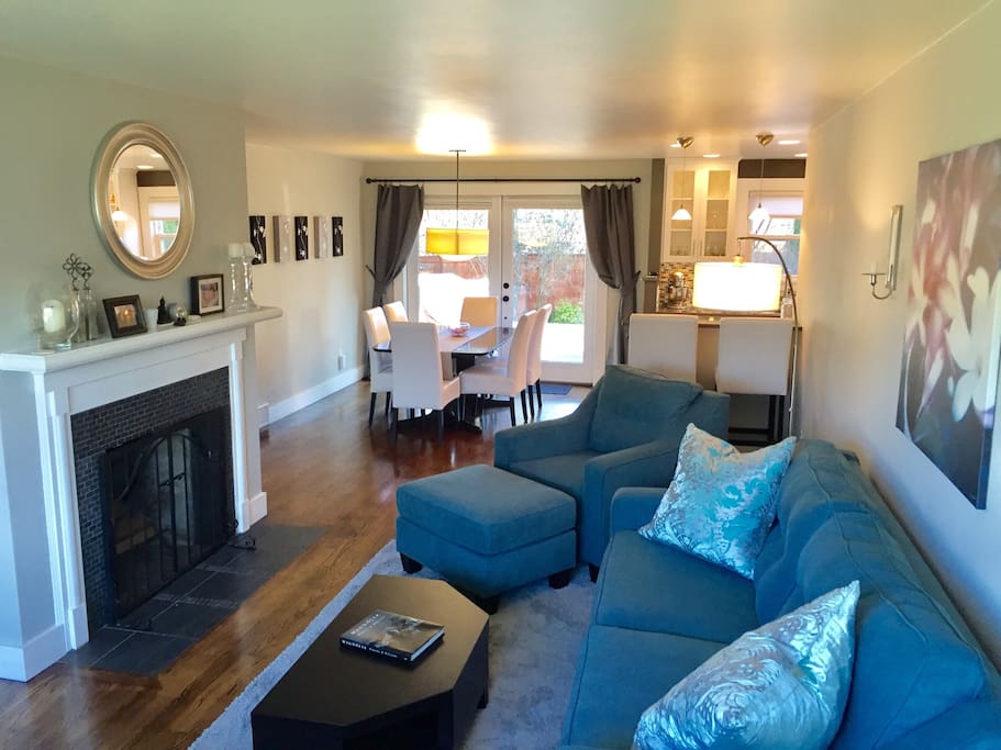 Living Room: Wood burning fireplace, sofa, love seat, armchair with ottoman, arched floor lamp, TV with DVD player. Dining Room: Dining table and leather chairs, seats six. French doors open to backyard deck. Two bar stools at kitchen bar.