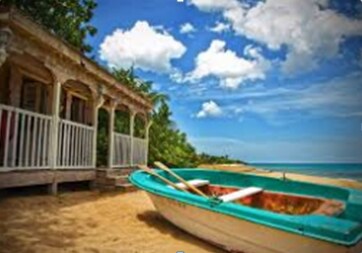 A small fishing boat rests in soft sand near a beachside bungalow. The vibrant blue boat is equipped with oars, while the charming structure features an inviting porch surrounded by tropical greenery. A clear blue sky with scattered clouds complements the serene coastal setting.