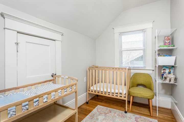 Un dormitorio luminoso y familiar con dos cunas, luz natural suave y suelos de madera cálida. Cuidadosamente organizado con asientos y almacenamiento acogedores, este espacio es ideal para familias que viajan con niños pequeños.