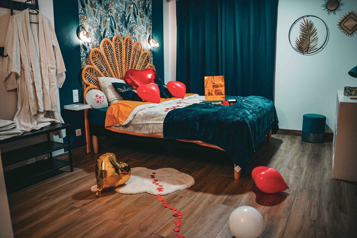 A cozy bedroom features a spacious bed with a decorative headboard, soft linens, and an assortment of colorful balloons. Warm lighting is provided by wall sconces, and a patterned wall adds character. A plush area rug sits on the wooden floor, completing the inviting ambiance.