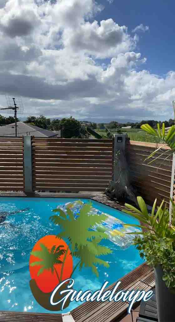 A private swimming pool featuring clear blue water is framed by wooden decking. Lush greenery can be seen along the perimeter, enhancing the outdoor setting. The backdrop showcases a scenic view of rolling hills under a partly cloudy sky.