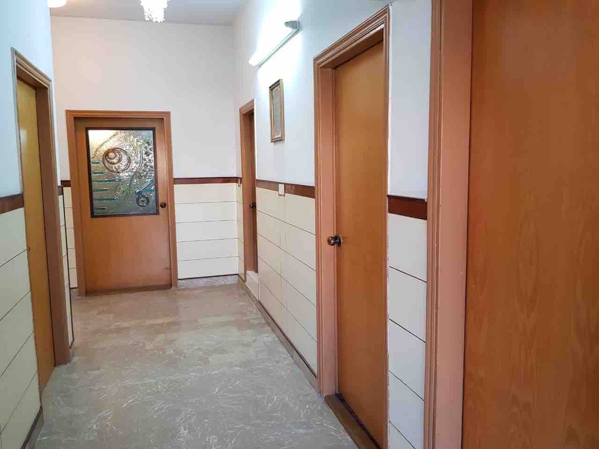 A well-lit hallway showcases a series of wooden doors leading to various rooms. The walls are adorned with a light color scheme accented by a darker trim. A decorative glass panel allows light to filter through near the end of the corridor.