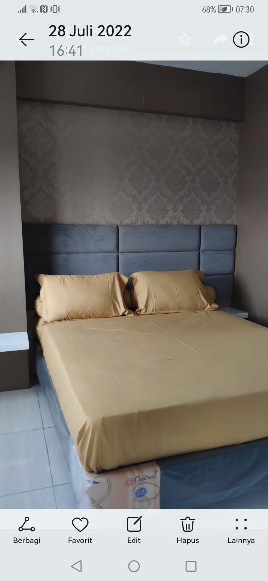 A spacious bed is dressed in a golden bedspread, with two matching pillows positioned neatly against a padded headboard. The walls feature a subtle patterned design, complementing the overall color scheme of soft grays and gold tones.