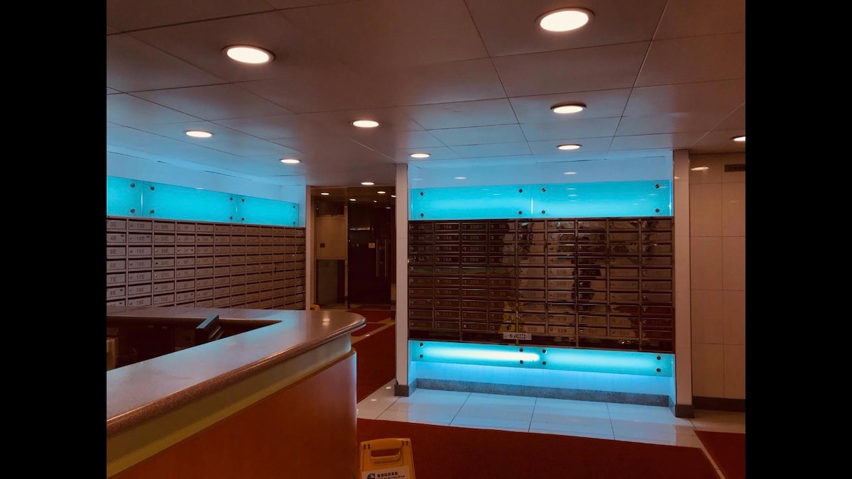 A modern lobby area features a reception counter and rows of secure mailboxes illuminated by soft blue lighting. The clean, bright space is accented with recessed ceiling lights, providing a welcoming atmosphere for residents and guests.