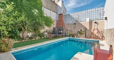 A refreshing swimming pool is surrounded by lush greenery and tiled walls. A trampoline is visible nearby, accompanied by a small play area. Natural light illuminates the space, with a patio area featuring seating options for relaxation.