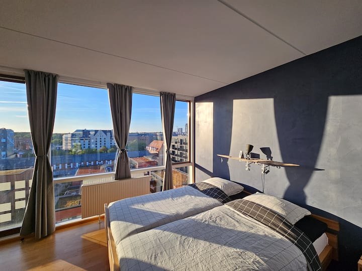 חדר שינה עם מיטת קינג סייז ווילונות האפלה עם נוף לקו הרקיע של האופק ממערב.