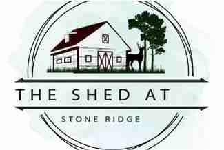 A circular logo featuring a stylized illustration of a building with a gable roof, flanked by trees and a deer. The text 'The Shed At Stone Ridge' encircles the image, highlighting the location.