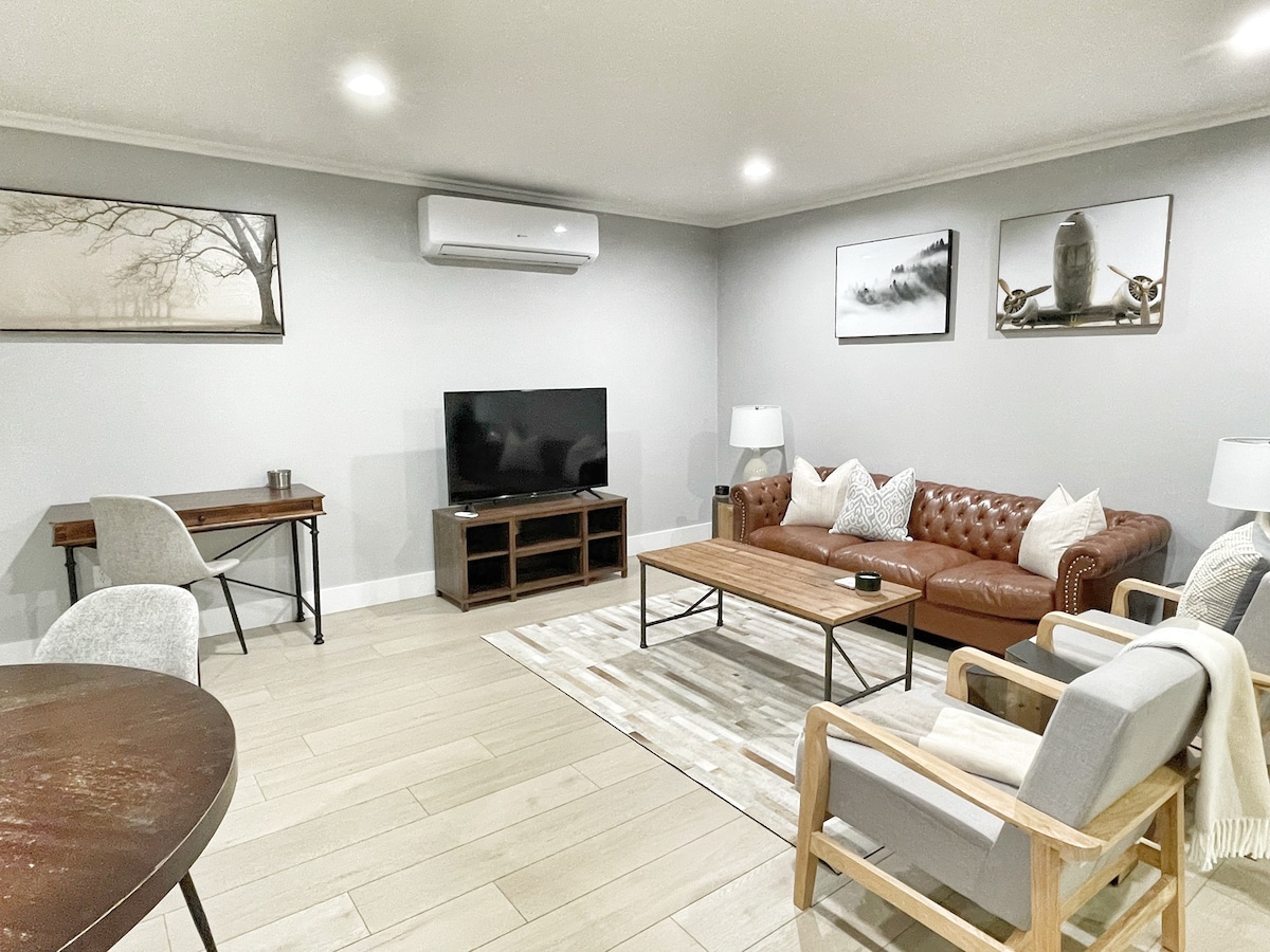 A welcoming living area features a comfortable leather sofa and armchairs arranged around a wooden coffee table. A wall-mounted flat-screen television sits opposite, while soft artwork adorns the walls. Ambient light casts a gentle glow, enhancing the modern yet rustic charm of the space.