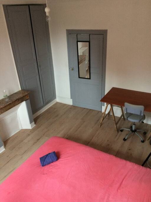 Chambre avec lit double, bureau, armoire, miroir.
