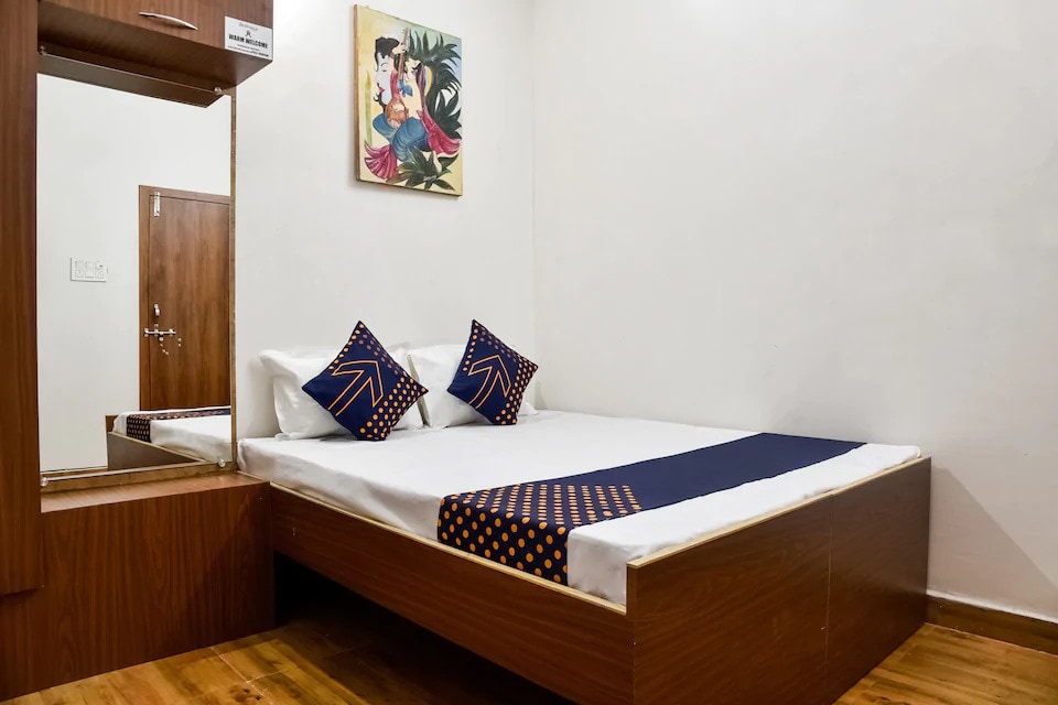 A well-furnished room features a spacious bed adorned with two decorative pillows. A mirror is positioned against the wall, reflecting the room's simplicity. Artwork depicting a woman is displayed above the bed, contributing to a pleasant decor.