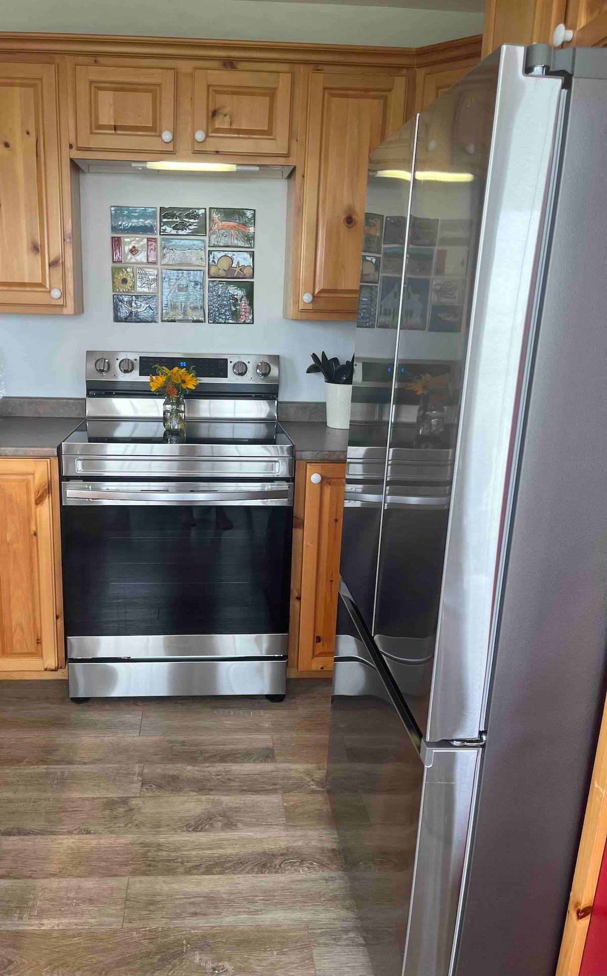 The kitchen features stainless steel appliances, including a stove and refrigerator. Wooden cabinetry provides a warm contrast to the sleek surfaces. A vase with fresh flowers sits on the countertop, adding a touch of color. A collection of framed images decorates the wall above the countertop.