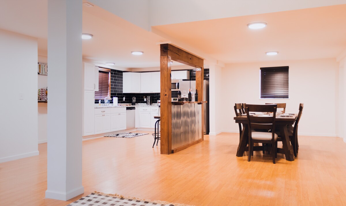 The open concept living area features a dining table with six chairs, situated adjacent to a modern kitchen equipped with white cabinetry and stainless appliances. Soft lighting illuminates the bamboo flooring, which extends throughout the space, creating a bright and functional environment.