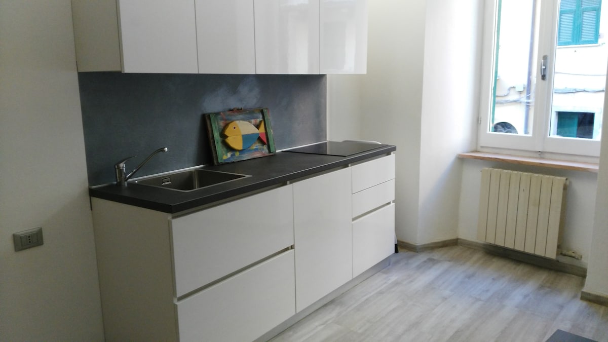 The kitchen area features modern white cabinetry and sleek countertops. A double sink is positioned under a window, allowing natural light to illuminate the space. A colorful framed artwork is displayed on the wall, adding a touch of visual interest.