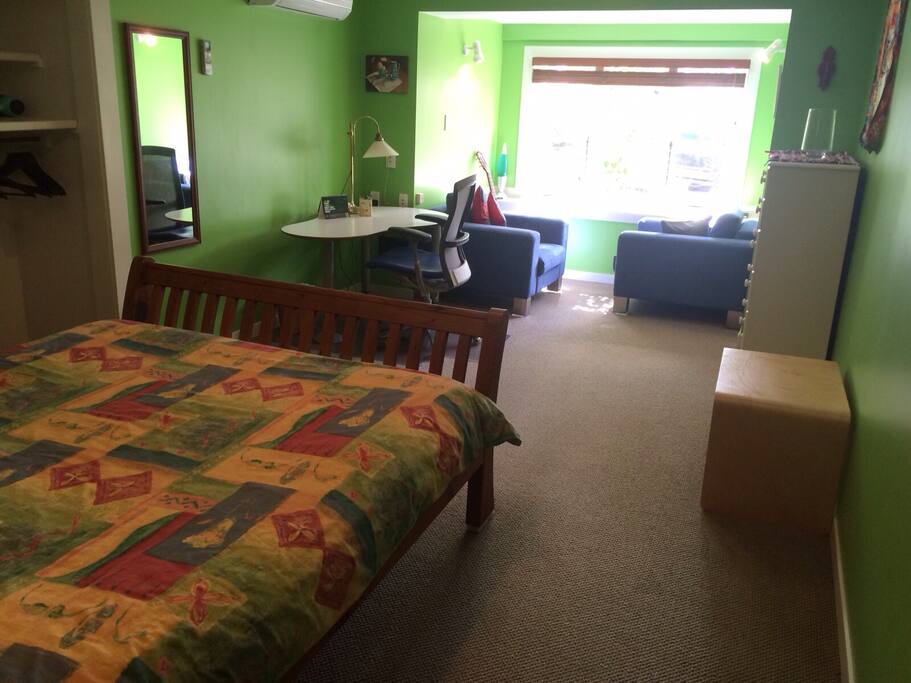 Large bedroom with a queen sized bed, work desk and chair, chest of drawers, full length mirror and two comfy lounging chairs.