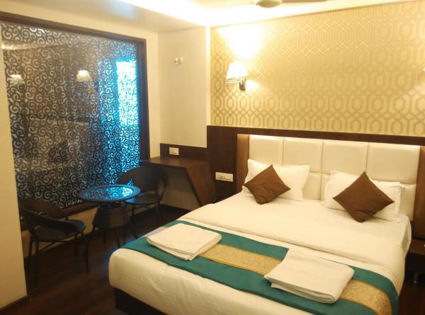 A well-appointed room features a spacious bed with decorative pillows, complemented by a light-colored bedspread. A small table and two chairs are positioned near a window adorned with patterned curtains. Soft lighting enhances the warm ambiance of the space.