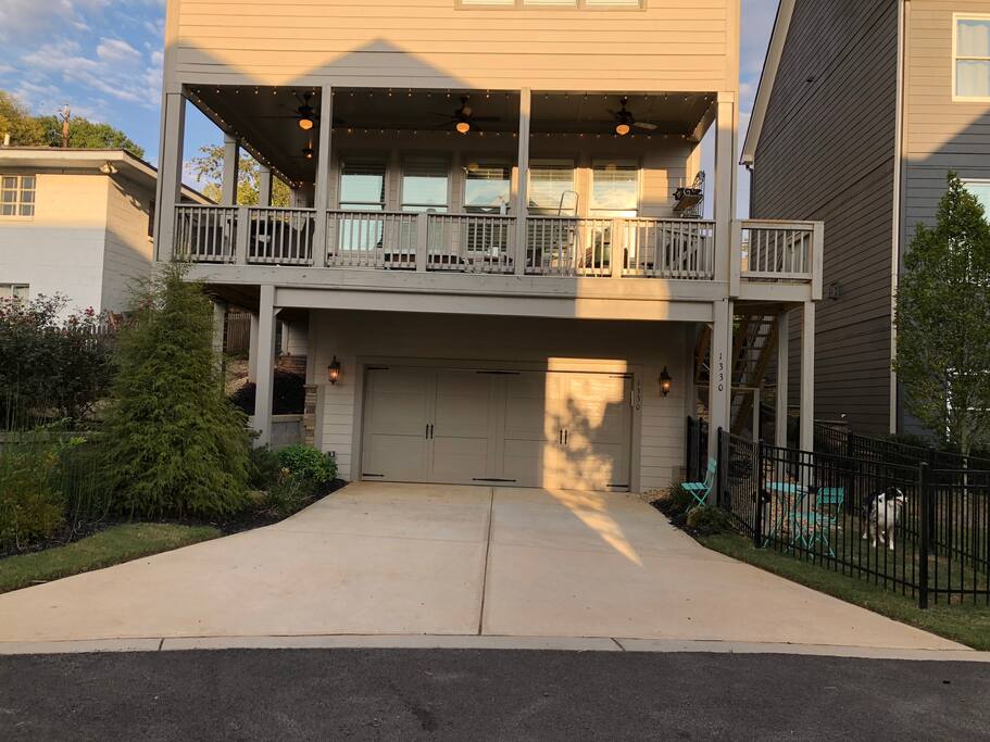 Rear property view where suite is accessed! Please be sure you are at the right location! Long drive, long covered porch wrapped with Edison lights and stairs; ; garden area to the left; black fenced yard to right with bright blue table and chairs