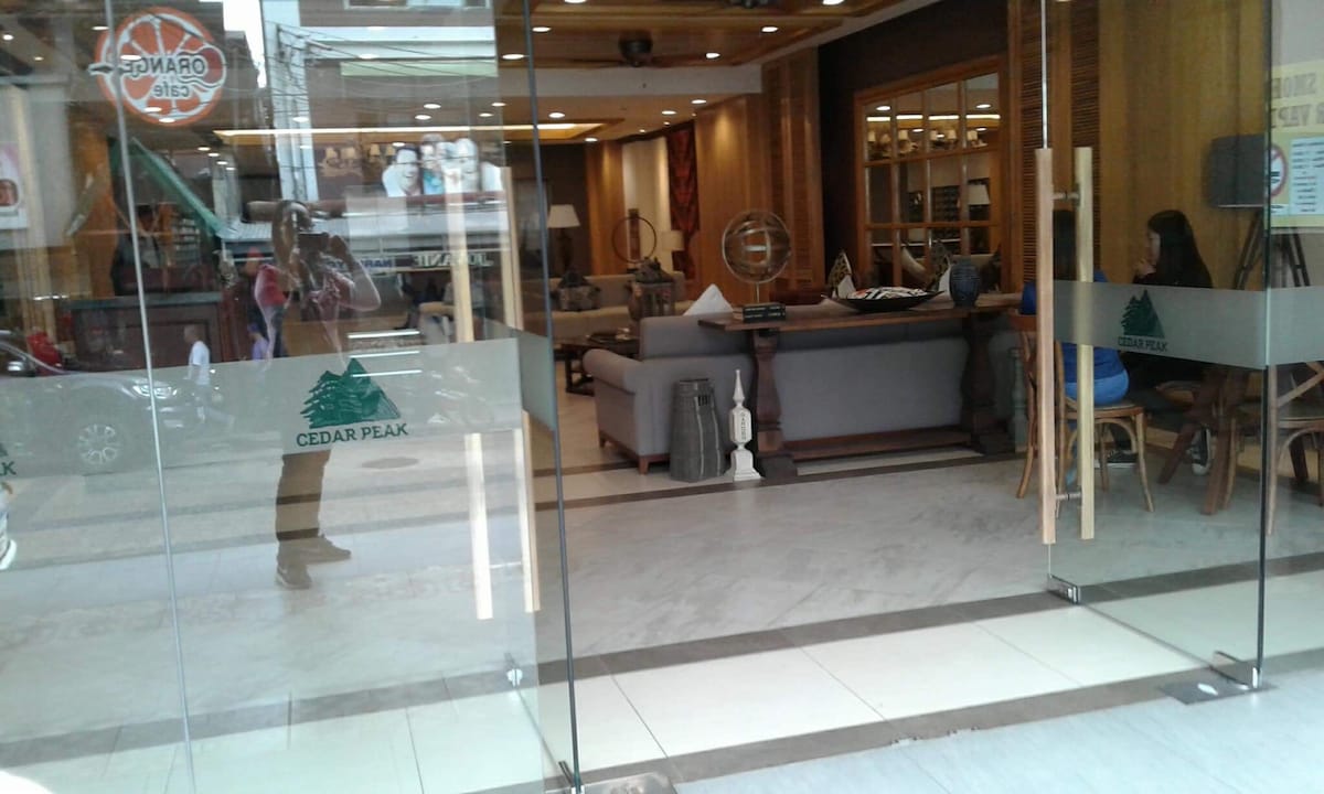 A modern lobby is highlighted by large glass doors, featuring cozy seating arrangements with neutral-toned sofas and wooden furniture. Soft lighting creates a welcoming atmosphere, and decorative elements such as vases and artwork can be seen in the background.