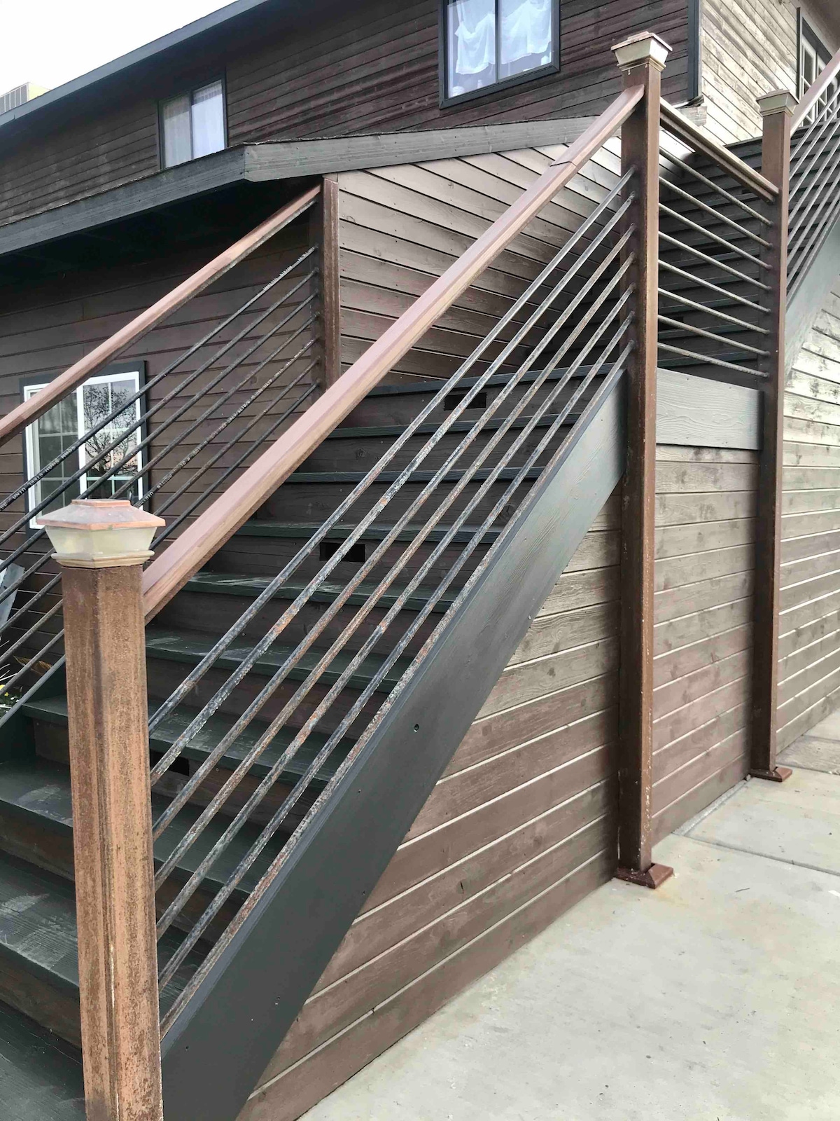 A set of exterior stairs is presented, leading to the upper floor of a rustic wooden barn. The staircase features metal railing for safety and is bordered by wood paneling. Natural light reflects off the surfaces, highlighting the warm tones of the wood.