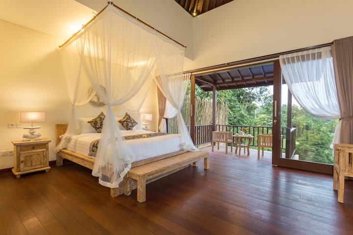 Romantic bedroom with a four-poster bed draped in sheer white fabric, creating an ethereal ambiance.  The room opens onto a private balcony with lush green views.