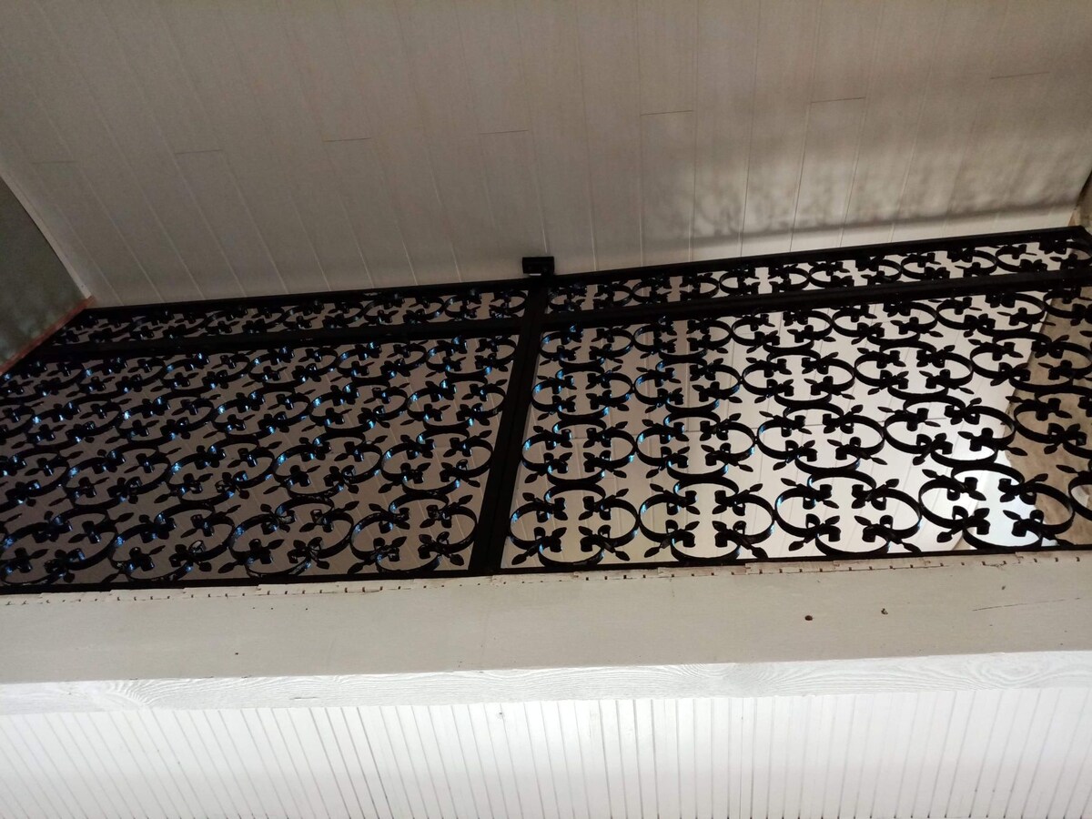 An intricate wrought iron balcony railing features a detailed floral design, displaying an elegant pattern. The railing provides a visual link between spaces, allowing for natural light to filter through while adding character to the room.