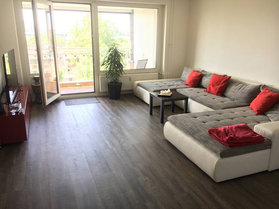 Wohnzimmer mit ausziehbarer Riesen-Couch und Zugang zum Balkon