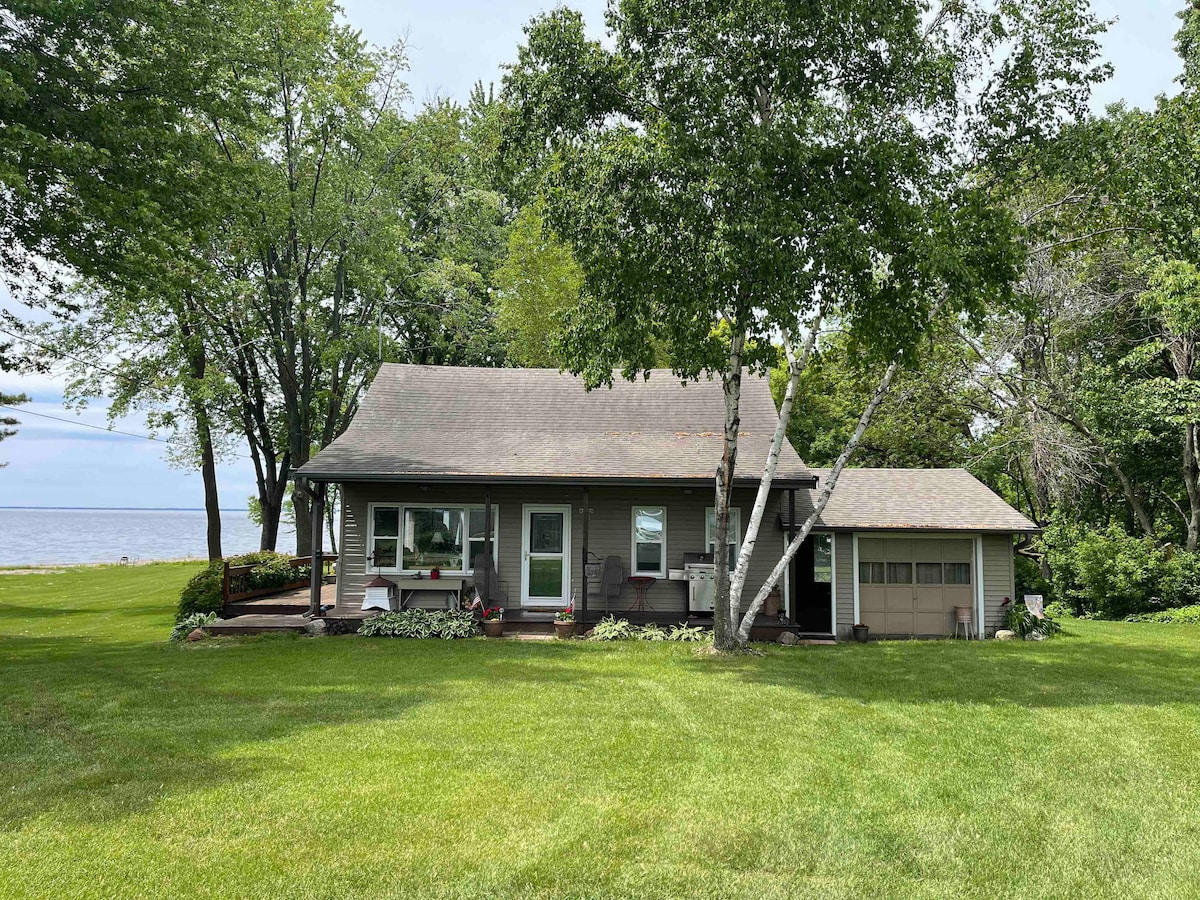 The exterior of the home is showcased, surrounded by lush greenery and mature trees. A spacious yard with well-maintained grass leads to the lake. The structure features a covered porch, a garage, and large windows, inviting ample natural light.