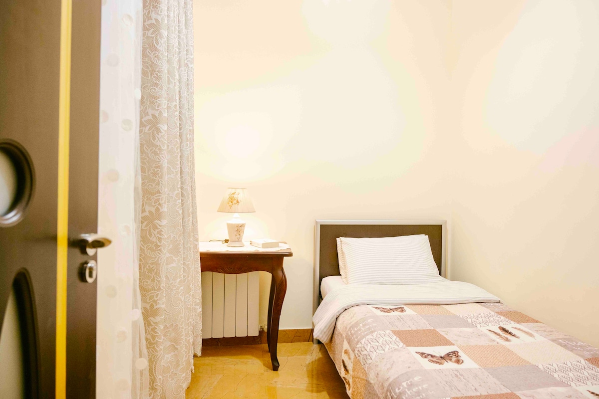 Chambre : lit simple, table, armoire, fenêtre donnant sur le salon, chauffage. 