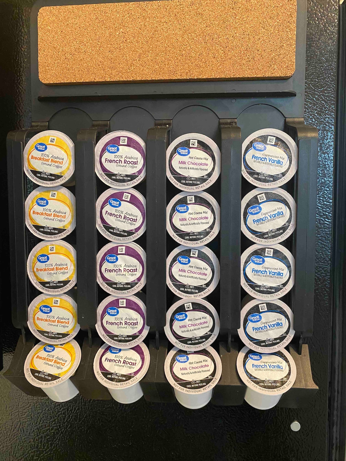 A coffee pod storage system is mounted on a black refrigerator. The system holds an assortment of coffee pods in various flavors, including French Roast, Milk Chocolate, and Vanilla. Each pod is clearly labeled, offering convenient access for coffee enthusiasts.