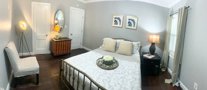 Chumba cha kulala #2 Queen chumba cha kulala.  Imewekwa na mapazia ya rangi ya Khaki.  Taa ya kiunzi cha miguu, kitambaa kidogo chekundu na cha dhahabu. Kiti cha kukaa cha Parson.