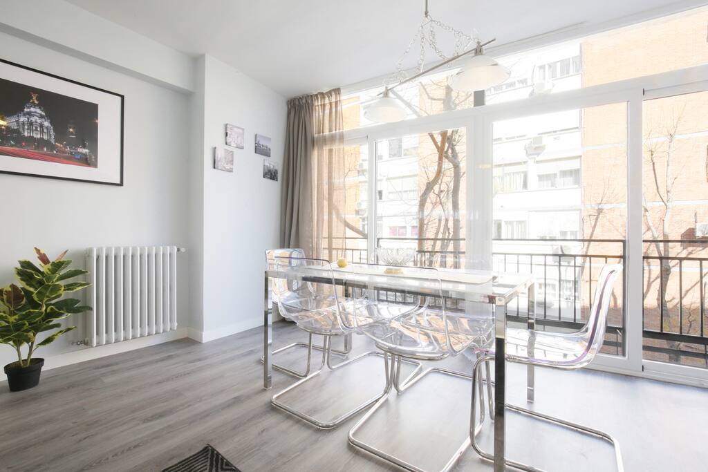 Zona de comedor con mesa y sillas de diseño, transparentes. Con amplios ventanales que van del suelo al techo de climalit dando una gran luminosidad y aislamiento térmico y acústico.